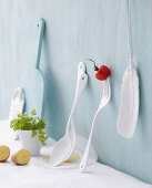 An arrangement of white cutlery and porcelain feather against a pastel blue wall