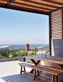 Holztisch und Bank auf überdachter Terrasse mit Meerblick
