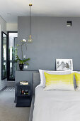 Kopfkissen mit gelbem Farbakzent auf Doppelbett im Schlafzimmer mit grau getönter Wand