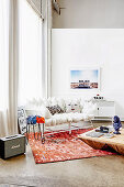 Weisses Kissen-Sofa auf rötlichem Teppich vor Fenster und Couchtisch aus Holz