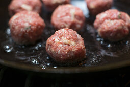 Raw meatballs being fried in a pan