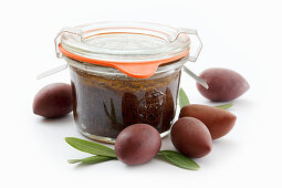 Homemade olive tapenade in a jar against a white surface