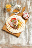 A tortilla topped with pork, coleslaw and vegetables