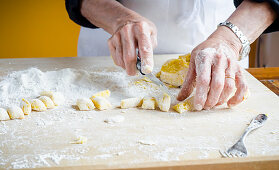 Italian chef cutting fresh homemade potato gnocchi into cubes with white flour on wooden board