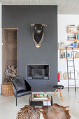 Cowhide rug, side table and black chair in front of bull's head on black wall above fireplace