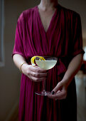 A woman in a dress holds a French 75 cocktail in her hands
