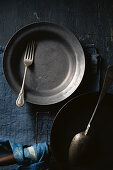 A black plate with a vintage fork, a pan, and a spoon against a blue background