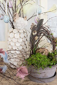Birch wreath decorated with quail eggs and feathers in planted bowl in front of Easter eggs hung from branches in vase