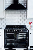 Black gas cooker and extractor hood on white subway wall tiles in kitchen