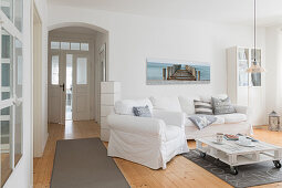 White, loose-covered sofa set, pallet coffee table and pale wooden floor in living room of converted dairy