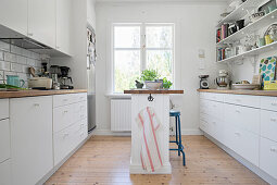 Narrow island counter in white kitchen with open shelving