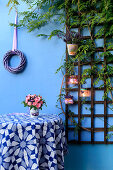 Posy in small bucket on table below wreath and trellis on wall decorated with handmade candle lanterns