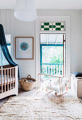 Mobile and baby cradle in front of balcony door and cot with canopy in baby room