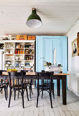 Dining table and chairs in kitchen with blue lacquered closet and vintage shelf