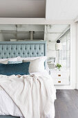 Double bed with high headboard in front of mirrored wall