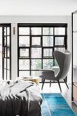 Doppelbett, Beistelltisch und Ohrensessel im Schlafzimmer mit Industriefenster