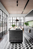 Black kitchen unit with green wall tiles and kitchen island in open kitchen with industrial window