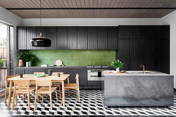 Black kitchenette with green wall tiles, concrete kitchen island and dining area