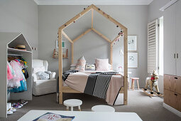 Himmelbett mit hausförmigem Holzgestell und offener Kleiderschrank im Mädchenzimmer mit hellgrauen Wänden