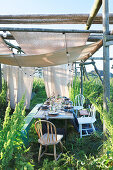 Table set for summer party below wooden frame covered with fabric awnings