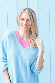 A young blonde woman wearing a blue jumper over a pink top