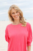 A young blonde woman on a beach wearing a pink top