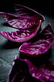 Chopped purple cabbage leaves scattered in a row on a black slate countertop
