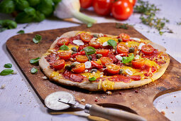 Vegetable pizza with tomatoes, chilli and capers on a pizza paddle