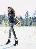 Junge Frau in Jeans, Streifenpulli und Kunstfellweste im Schnee