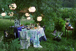 Set table and chair with matching covers below illuminated lanterns in garden