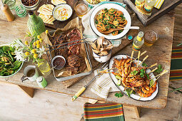 Gedeckter Tisch mit gegrilltem Fleisch, Garnelen, Süsskartoffeln und Salat (Italien)