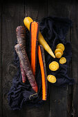 Rainbow carrots on a cloth against a wooden background (top view)