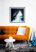 Yellow upholstered sofa with fur pillows, white side table and pyramid set, large-format photography on wall