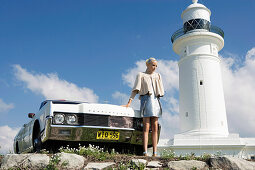 A blonde woman wearing a silver dress and a naturally white jacket standing by a car