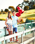 A young couple with a red, heart-shaped balloon by a lake
