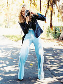 A blonde woman wearing a dark blue blazer and light blue jeans with a camera