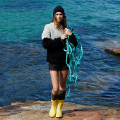 A brunette woman wearing a knitted jumper, short and wellie boots holding a fishing net