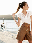 A young woman by the sea wearing a white blouse and brown culottes