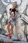 A blonde woman wearing a printed dress standing in front of a graffitied wall