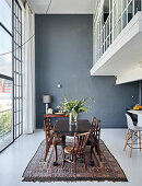 Dining table and chairs next to glass wall in high-ceilinged room