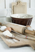 Various baking utensils, flour, eggs and milk on a wooden chopping board