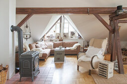 Log burner, wing back chair and corner sofa in cosy living room with wooden beams