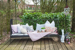 Cushions, blanket and wicker tray on garden bench and rabbit ornament on terrace