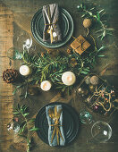 Christmas or New Years eve holiday table setting: Flat-lay of plates, silverware, glassware, candles, olive branches and toy festive decorations