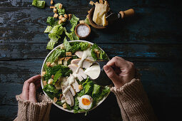 Female hands powring dressing to Classic Caesar salad with chicken breast in white ceramic plate