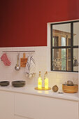 Illuminated bottles in kitchen with red wall and interior window