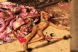 Blonde Frau im Bikini liegt im Sand