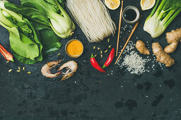 Asian cuisine ingredients over dark slate stone background, vegetables, spices, shrimp, rice, sauces for cooking vietnamese, thai or chinese food