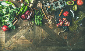 Winter vegetarian, vegan food cooking ingredients, seasonal vegetables and fruits, beans, cereals, kitchen utencils, dried flowers, olive oil over wooden background