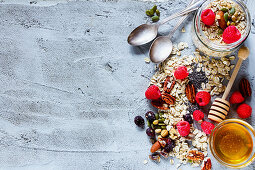 Colorful ingredients for cooking breakfast or smoothie (fresh berries, nuts, oat flakes, dried fruits, chia seeds and honey) over concrete textured background